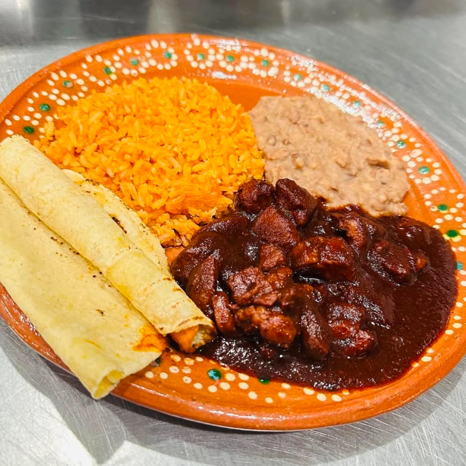 Taqueria Monterrey's mole poblano with rice, refried beans, and tortillas on a decorative orange plate.
