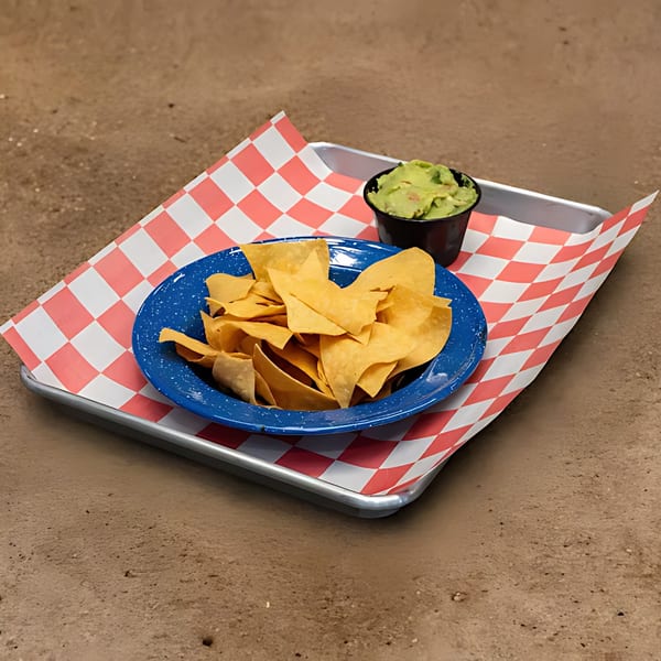 A blue plate of tortilla chips and a small black cup of guacamole on a checkered paper-lined tray.