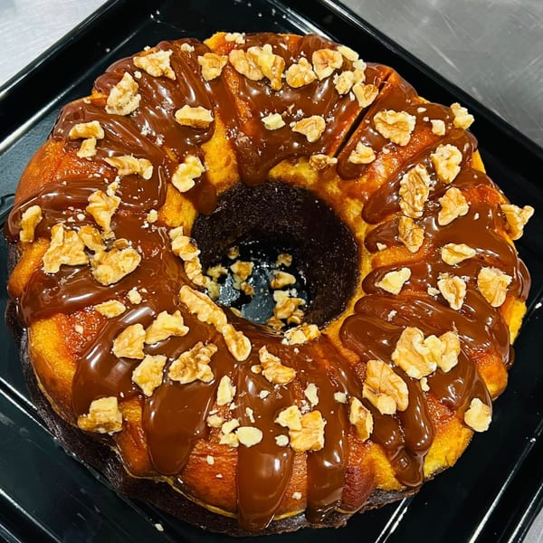 A bundt cake with chocolate drizzle and walnuts on a black tray.