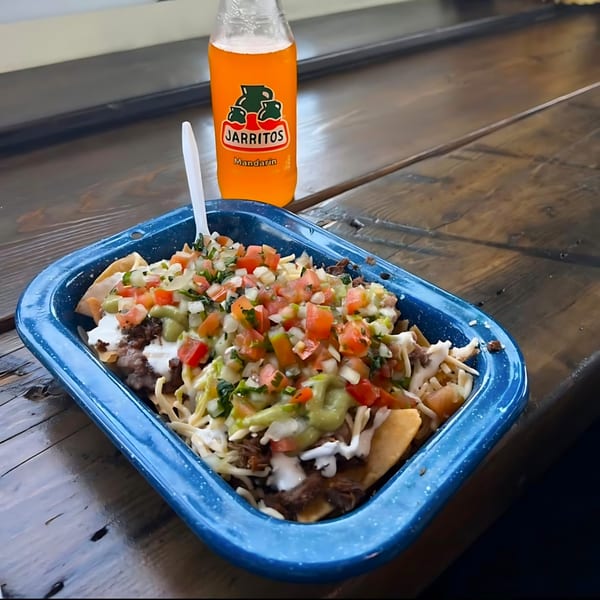 Nachos with meat, cheese, salsa, and guacamole in a blue dish, with a Jarritos soda.