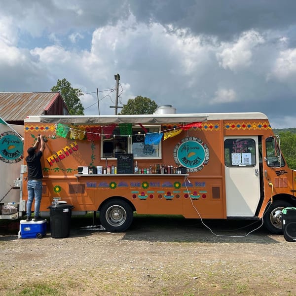 A person decorates the orange Taqueria Monterrey food truck with colorful papel picado banners.