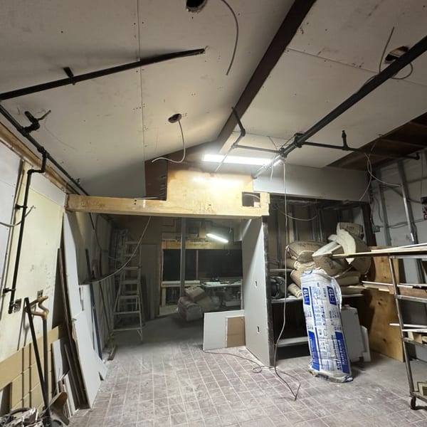 An unfinished restaurant interior with exposed pipes, drywall, insulation, and construction materials.