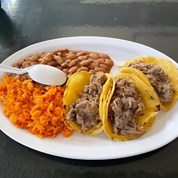 Three carnitas tacos with a side of orange rice and pinto beans on a white plate.