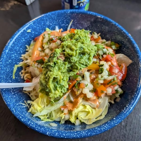 Taco salad with guacamole, pico de gallo, and dressing in a blue speckled bowl.