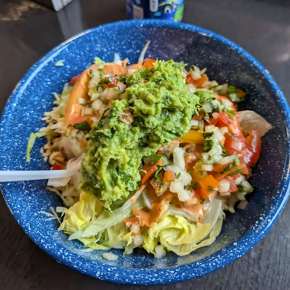 Taco salad with guacamole, pico de gallo, and dressing in a blue speckled bowl.