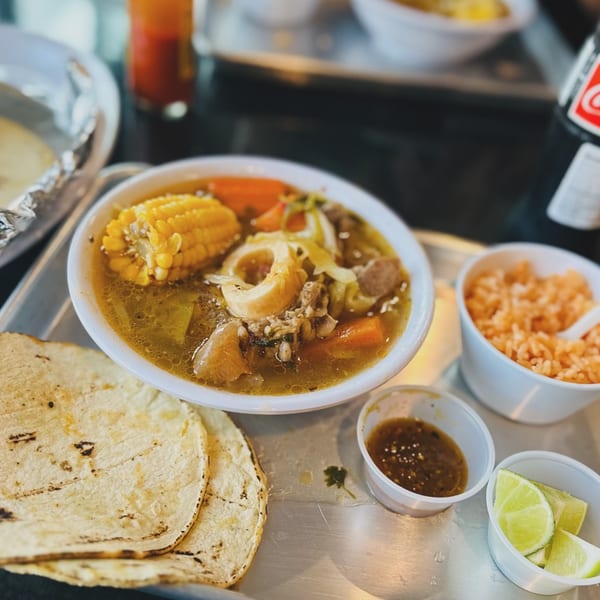 A bowl of Taqueria Monterrey's beef soup with corn, carrots, and tortillas on a tray.