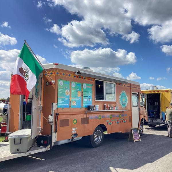 Taqueria Monterrey food truck, orange with a Mexican flag, under a blue sky with clouds.