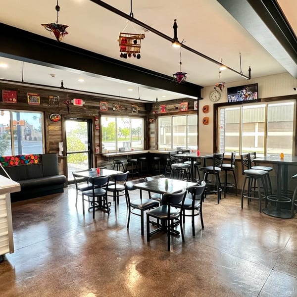 Interior of Taqueria Monterrey with wooden walls, black tables, chairs, and bar stools, and large windows.
