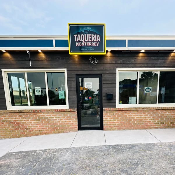 Exterior of Taqueria Monterrey, a restaurant with a dark wood facade, brick base, and a bright yellow sign.