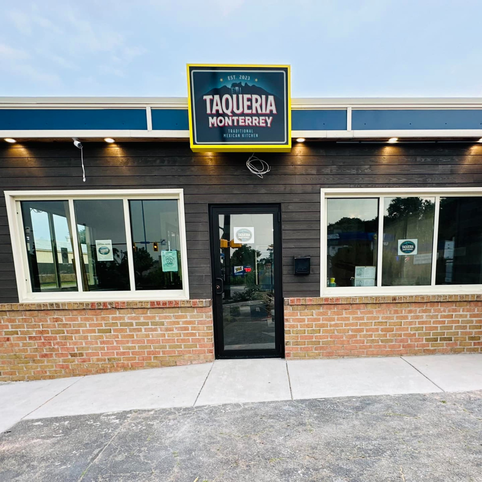 Exterior of Taqueria Monterrey, a restaurant with a dark wood facade, brick base, and a bright yellow sign.