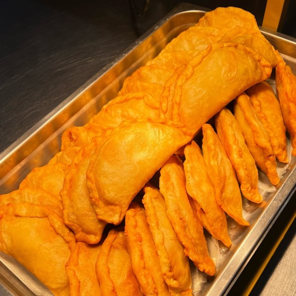A metal tray filled with many golden-brown, fried empanadas, some large and some small.