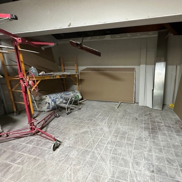 Construction materials, including drywall sheets and scaffolding, in a room with tiled floors.